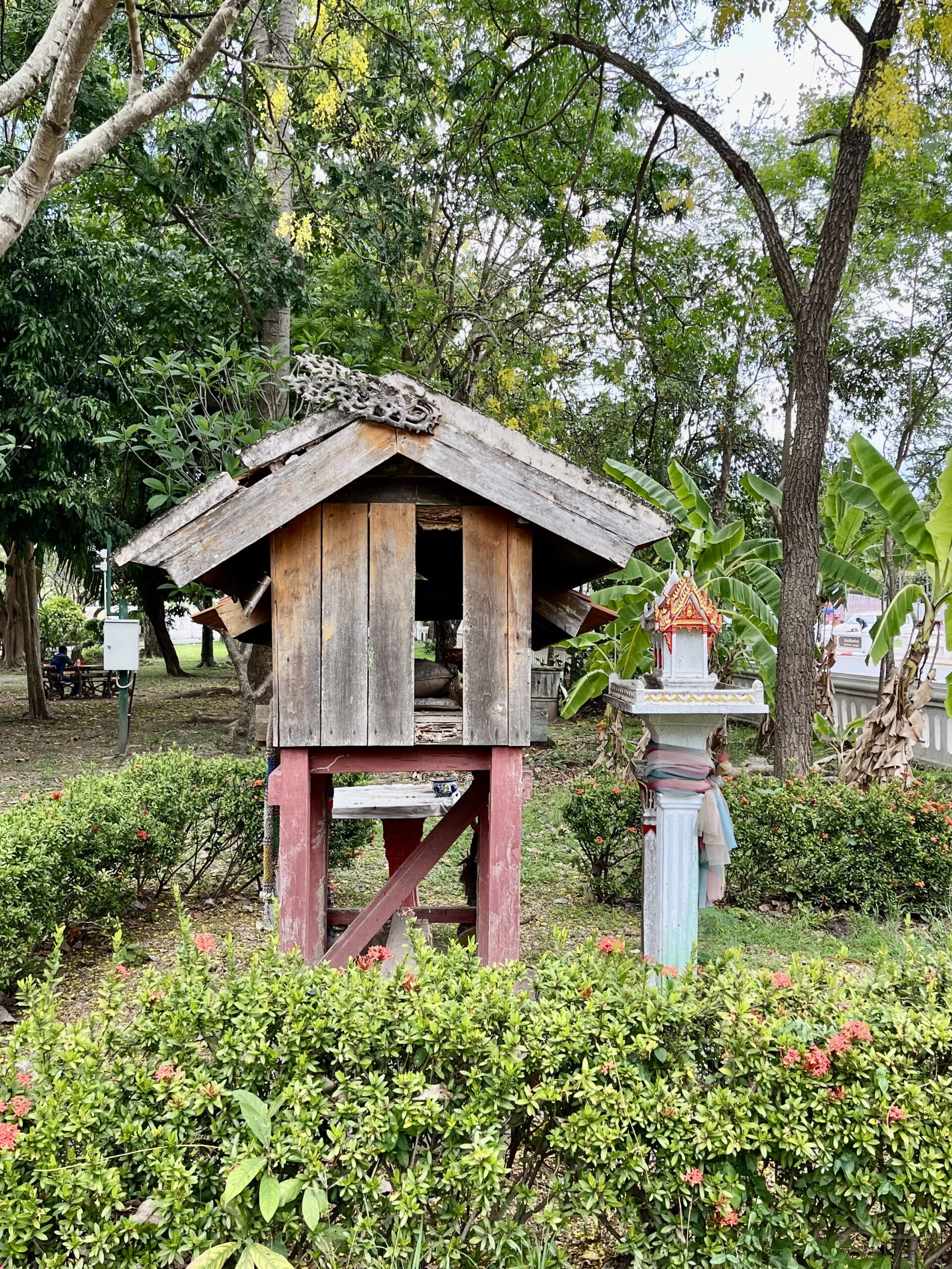 The back of a wooden shrine ressembling a house in a garden with one panel missing