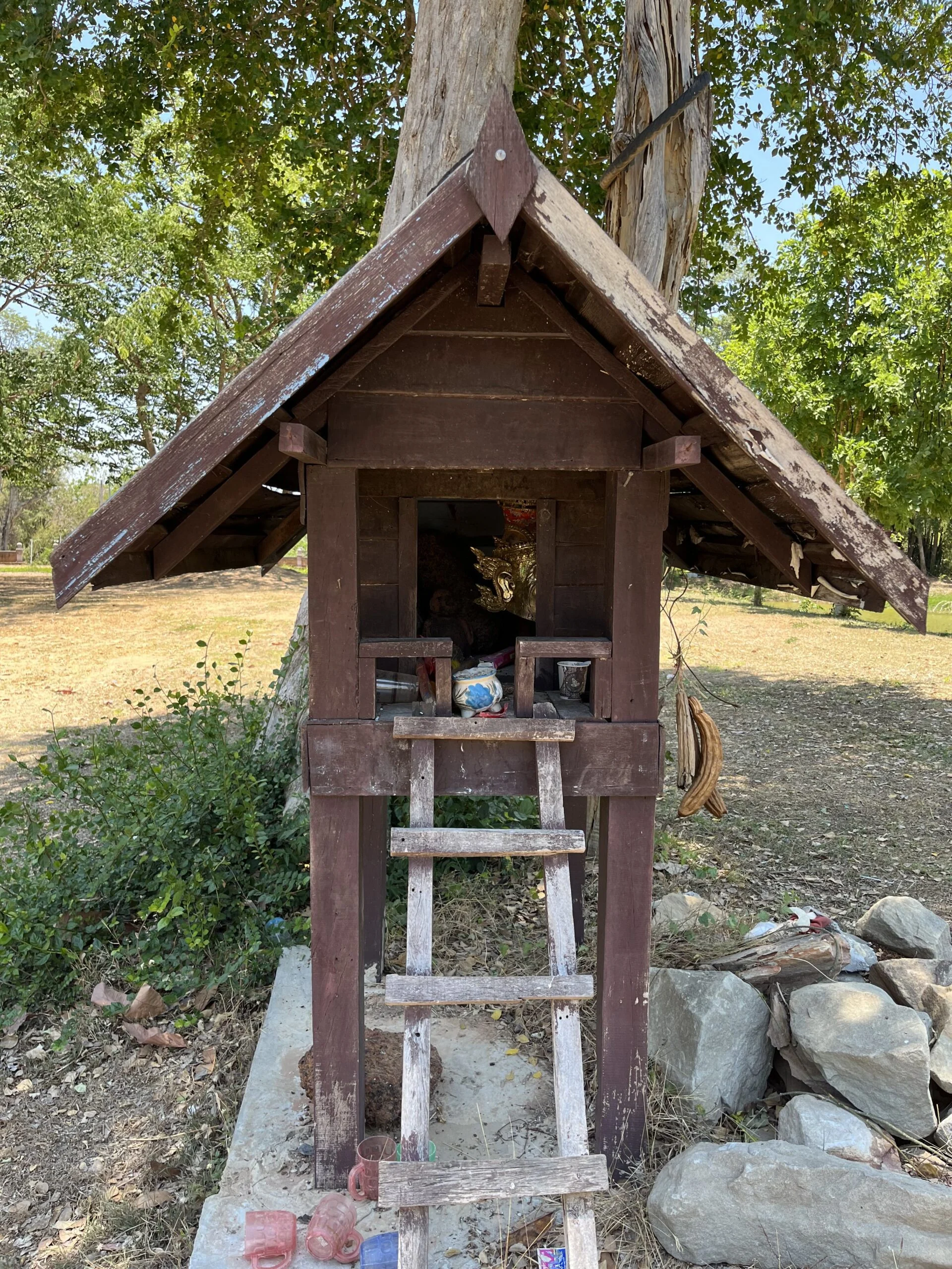 A brown wooden shrine resembling a simple house with a triangular roof with a ladder leading up to the entrance.