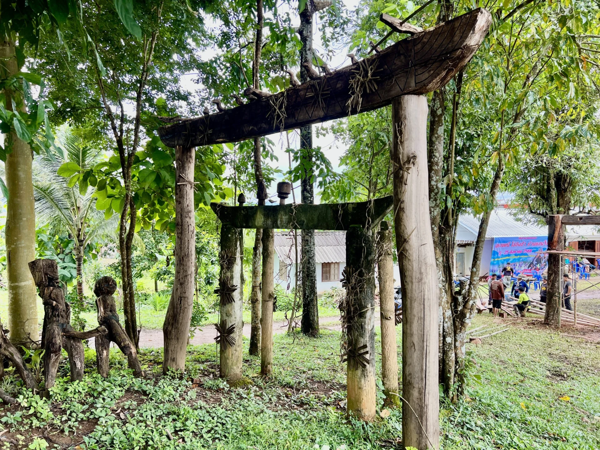 Two gates made up of a post on either side and a post with ends curving upwards across the top. The larger gate is in front, and the smaller gate, half the size, is slightly behind. On the edge, a small human-like statue is visible. There is grass on the ground and trees in the background.