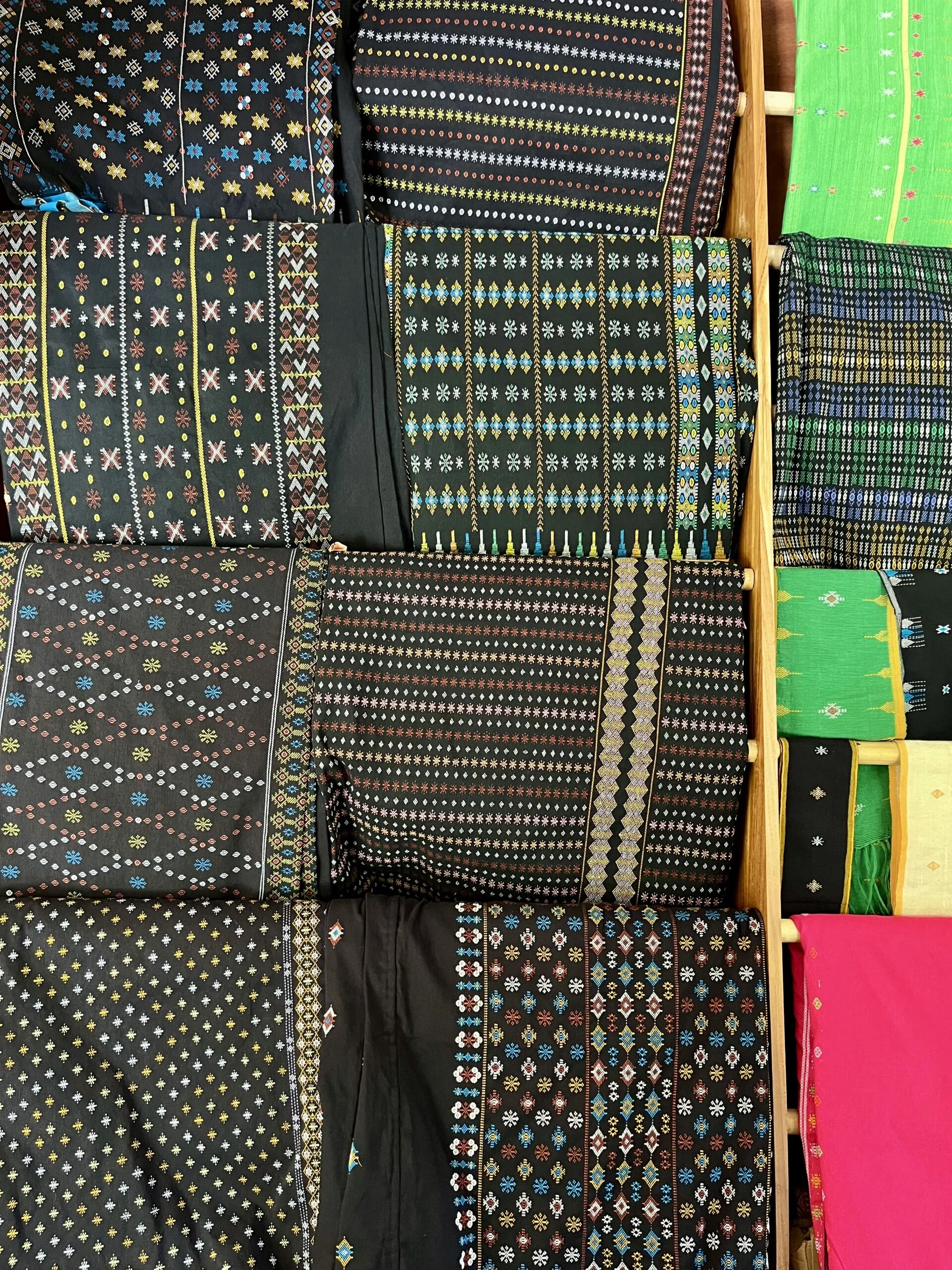 Folded sheets of black fabric with patterns embroidered in different bright colours.