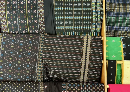 Folded sheets of black fabric with patterns embroidered in different bright colours.